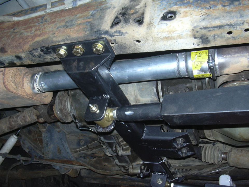 Underbody view of a custom suspension modification with yellow labels on exhaust pipe