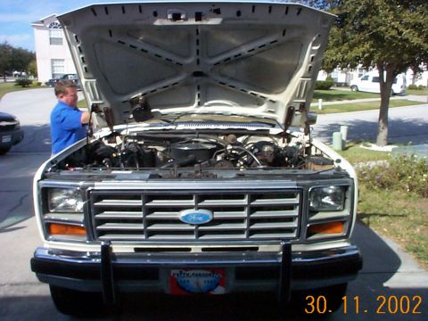 1985 Ford Bronco - Front view of a white Ford truck with its hood open, revealing the engine bay and a prominent chrome grille.