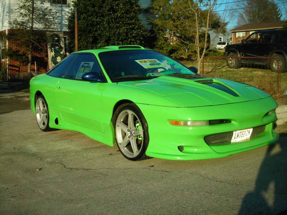 Lime green sports coupe with custom body kit and aftermarket wheels. Has a 'For Sale' sign in the windshield