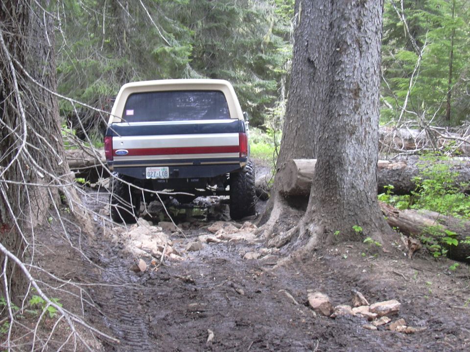 1991 Ford Bronco rear view on muddy forest trail. License plate reads 027-L08
