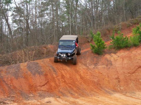 1993 Ford Bronco - A dark blue Jeep Wrangler TJ navigates an off-road trail with a tan soft top.