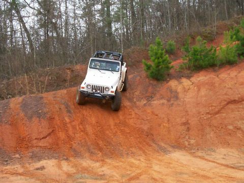 1993 Ford Bronco - A white Jeep Wrangler navigates a steep, red dirt trail surrounded by trees.