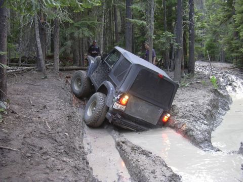 1991 Ford Bronco - This Jeep Wrangler is navigating a challenging muddy trail with steep inclines and deep ruts.