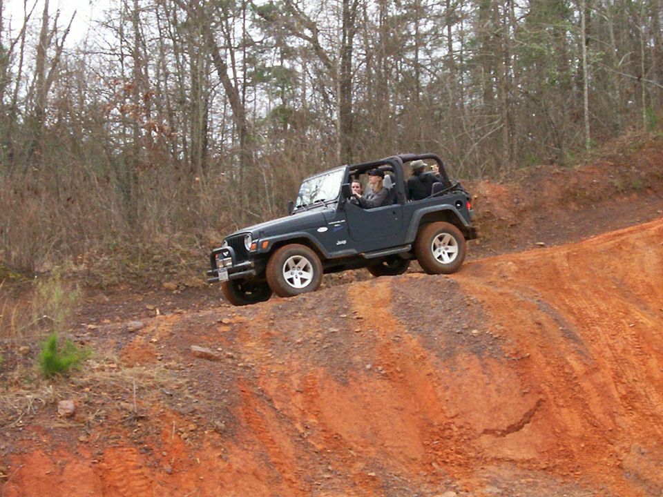 Dark blue Jeep Wrangler driving on a dirt hill with trees in the background