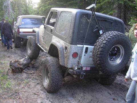 1991 Ford Bronco - Off-road vehicles navigate a challenging muddy trail, encountering obstacles like a fallen log.