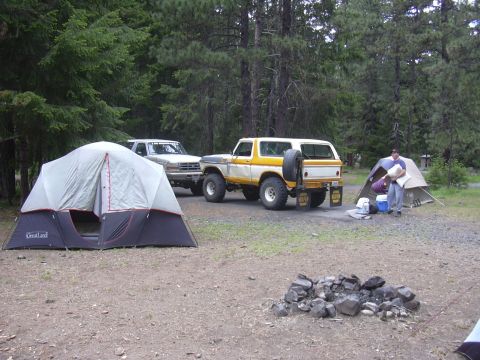 1991 Ford Bronco - Two Ford SUVs are parked at a campsite with tents and a fire pit.