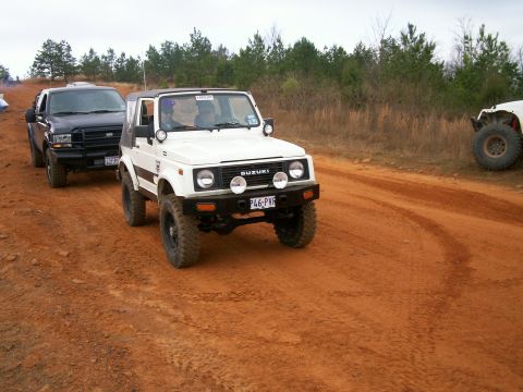 1993 Ford Bronco - A white Suzuki Samurai drives on a dirt track, with another SUV following behind.