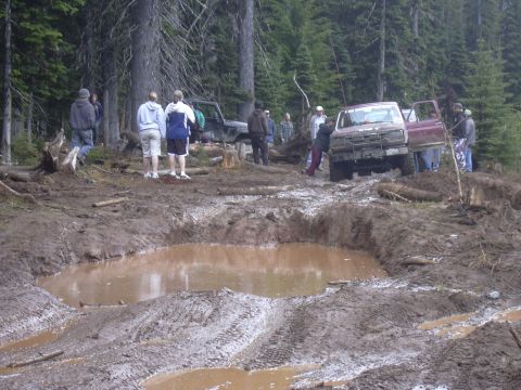 1991 Ford Bronco - A group of people gather around a maroon 1991 Ford Bronco that is stuck in a muddy off-road trail.