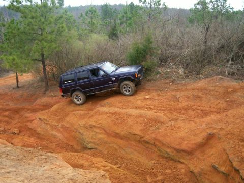1993 Ford Bronco - Jeep Cherokee XJ navigates a challenging off-road terrain with steep inclines and loose dirt.