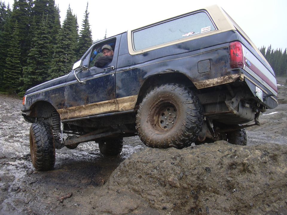 Driver in a 1991 Ford Bronco navigating a muddy, rocky trail