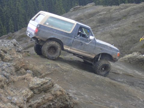 1991 Ford Bronco - A dark blue 1991 Ford Bronco navigates a steep, rocky terrain during an off-road excursion.