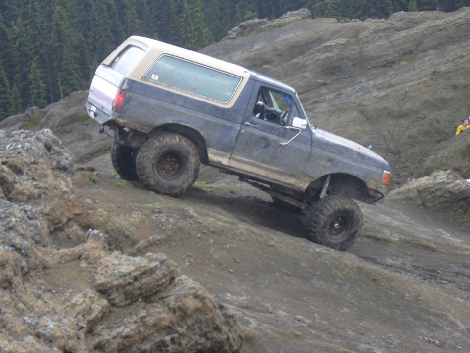 1991 Ford Bronco climbing a rocky incline, dark blue with tan top