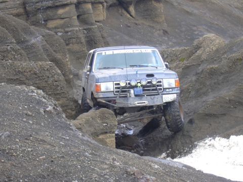 1991 Ford Bronco - This modified Ford Bronco is tackling a challenging off-road course with large rocks and water.