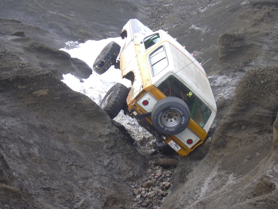 Yellow and white off-road vehicle tilted in a ravine, with one wheel off the ground