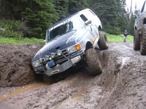 1991 Ford Bronco - This Ford Bronco is navigating a difficult muddy trail, with another vehicle following close behind.