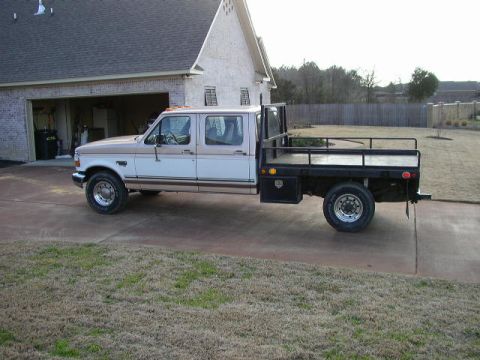 1995 Ford Bronco - Side view of a 1995 Ford F-350 Super Duty flatbed truck parked in front of a house.