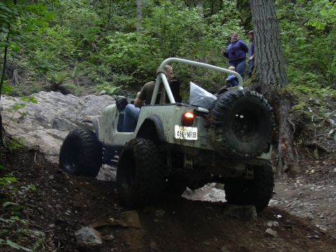 1991 Ford Bronco - A Jeep CJ-7 tackles a challenging rocky trail with passengers inside and onlookers nearby.