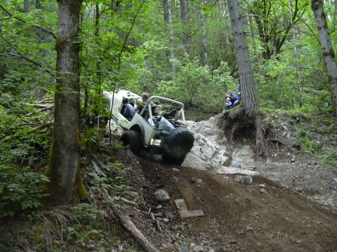 1991 Ford Bronco - An off-road Jeep navigates a steep, rocky trail surrounded by dense forest.
