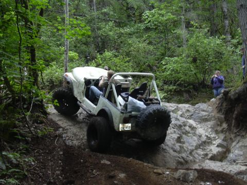 1991 Ford Bronco - A white off-road vehicle tackles a challenging rocky terrain in a wooded area.