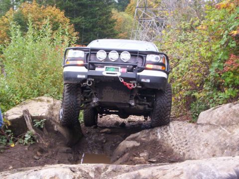 1991 Ford Bronco - Off-road truck with large tires and winch is climbing over rocks on a trail.