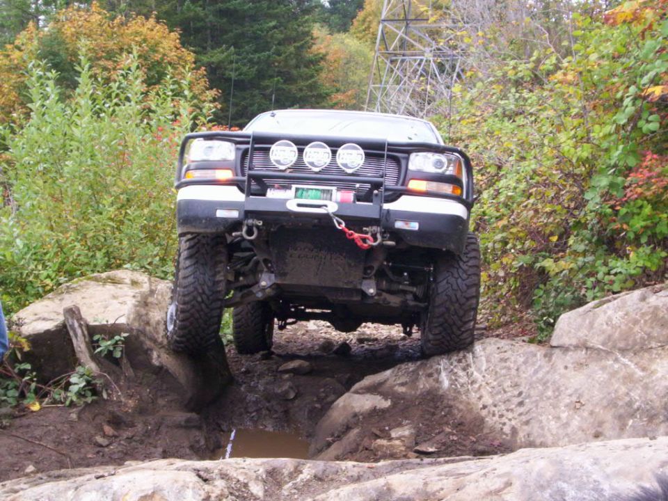 White off-road truck with winch and brush guard navigating large rocks