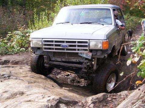 1991 Ford Bronco - A silver Ford Bronco navigates a challenging rocky terrain on an off-road trail.