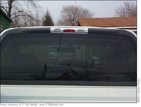 Rear cab window of a white pickup showing the third brake light and cargo lamp housing