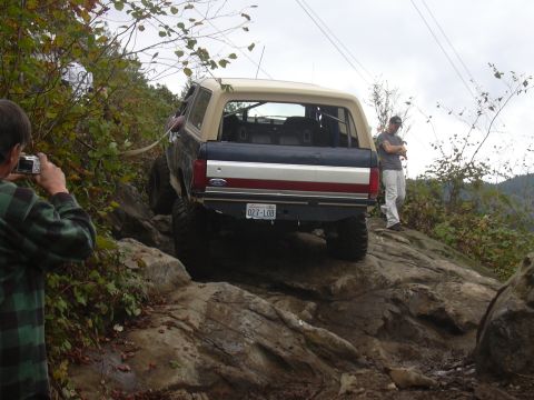1991 Ford Bronco - A Ford Bronco navigates a challenging rocky terrain, with a person photographing the scene.