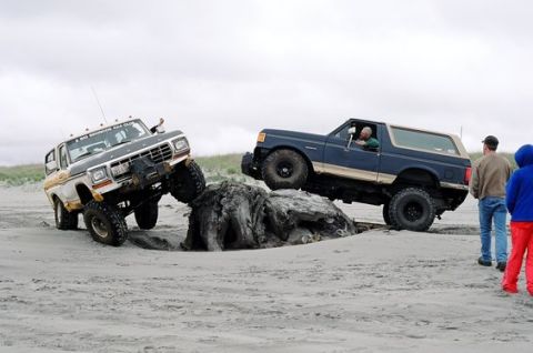 1991 Ford Bronco - Two Ford Broncos tackle driftwood on a sandy beach, demonstrating off-road capabilities.