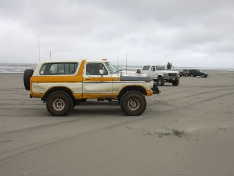 1991 Ford Bronco - A vintage two-tone SUV with a spare tire on the rear is seen on a beach alongside other vehicles.