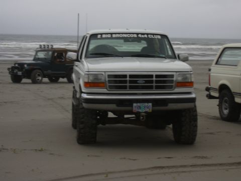1991 Ford Bronco - A white Ford Bronco is parked on a sandy beach with two other vehicles nearby.