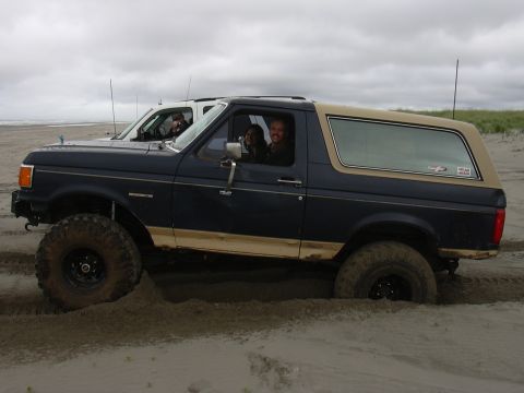 1991 Ford Bronco - Two vehicles on a beach, with the lead Ford Bronco partially stuck in the sand.