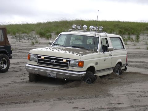 1991 Ford Bronco - A 1991 Ford Bronco is stuck in the sand dunes with its tires partially buried.