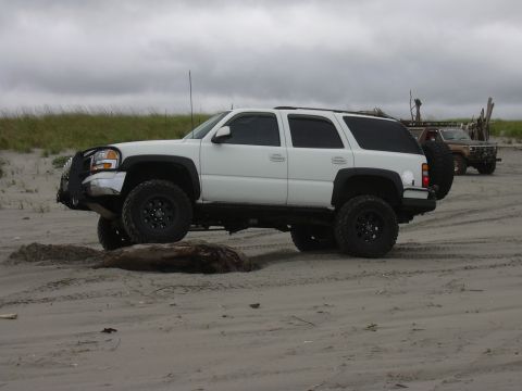 1991 Ford Bronco - A lifted white SUV navigates a sandy terrain, with a second vehicle visible in the distance under an overcast sky.