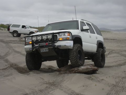 1991 Ford Bronco - Two SUVs on a sandy terrain under an overcast sky.
