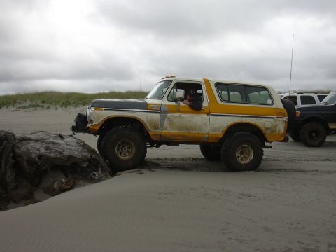 1991 Ford Bronco - This classic Ford Bronco is shown off-road on a sandy terrain with a cloudy sky overhead.