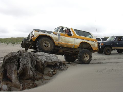 1991 Ford Bronco - A modified Ford Bronco navigates a sandy beach, with another truck visible in the background.