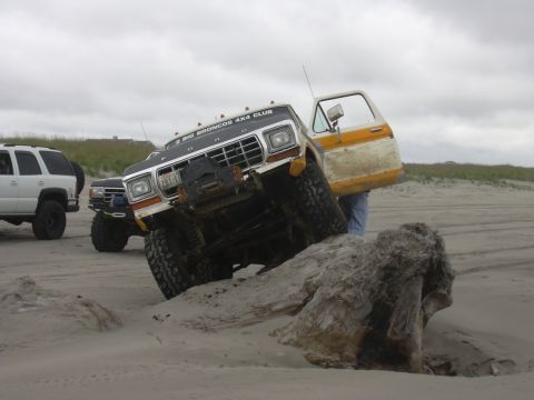 1991 Ford Bronco - A lifted Ford Bronco navigates a sandy dune, with another SUV and truck visible in the background.