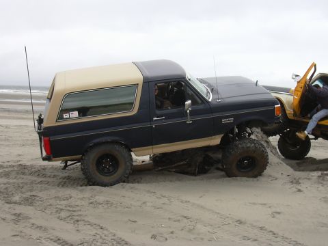 1991 Ford Bronco - A lifted 1991 Ford Bronco navigates a sandy beach, with another vehicle assisting.