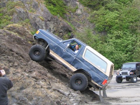 1991 Ford Bronco - A 1991 Ford Bronco navigates a steep, rocky incline on a beach, with another Jeep visible on the sand.
