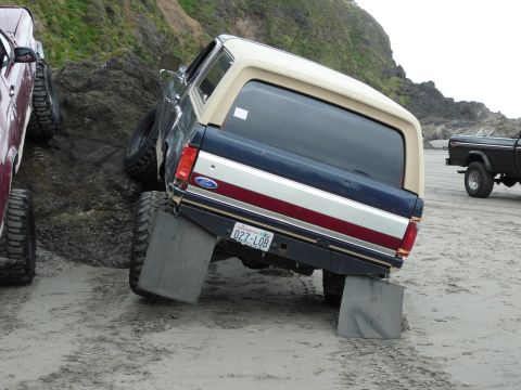 1991 Ford Bronco - A 1991 Ford Bronco is positioned on a rocky beach, with another vehicle visible in the background.