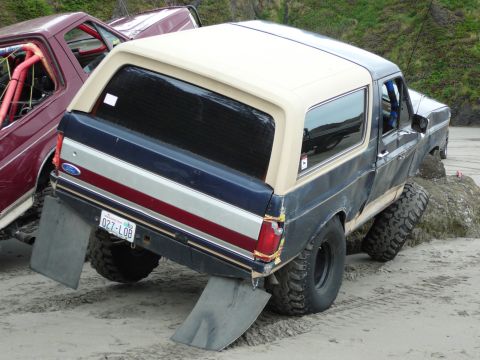 1991 Ford Bronco - Two off-road vehicles, including a 1991 Ford Bronco, parked on a sandy beach.