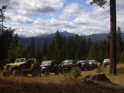 1991 Ford Bronco - A group of off-road vehicles are gathered in a scenic, wooded area under a cloudy sky.
