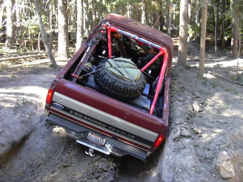 1991 Ford Bronco - A 1991 Ford Bronco 4x4 navigates a challenging off-road obstacle, tilted precariously in a ditch.