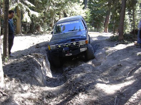1991 Ford Bronco - A dark blue Ford Bronco tackles a challenging muddy trail during an off-road event.