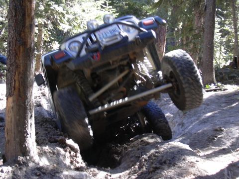 1991 Ford Bronco - An off-road vehicle navigates a challenging trail, tilted precariously in a deep rut.