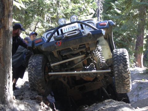 1991 Ford Bronco - Off-road Jeep Wrangler navigating a difficult dirt trail with assistance from bystanders.