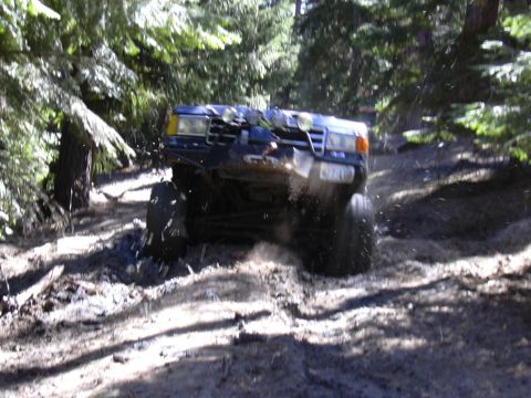 1991 Ford Bronco - A modified off-road vehicle navigates a muddy path through a forest.