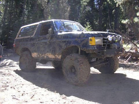 1991 Ford Bronco - This heavily modified 1991 Ford Bronco is shown off-road, covered in mud and equipped with large tires and auxiliary lighting.