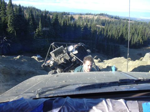 1991 Ford Bronco - An off-road vehicle is stuck on a steep, muddy slope in a wooded area, with another vehicle's dashboard visible in the foreground.